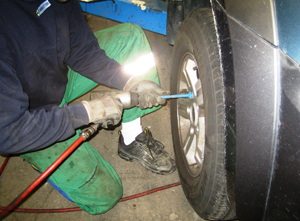 En mand skifter d�k p� en bil med et v�rkt�j i h�nden