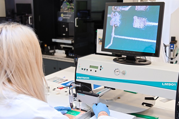 An electrical engineer sits at a pick and place machine working on a PCB board