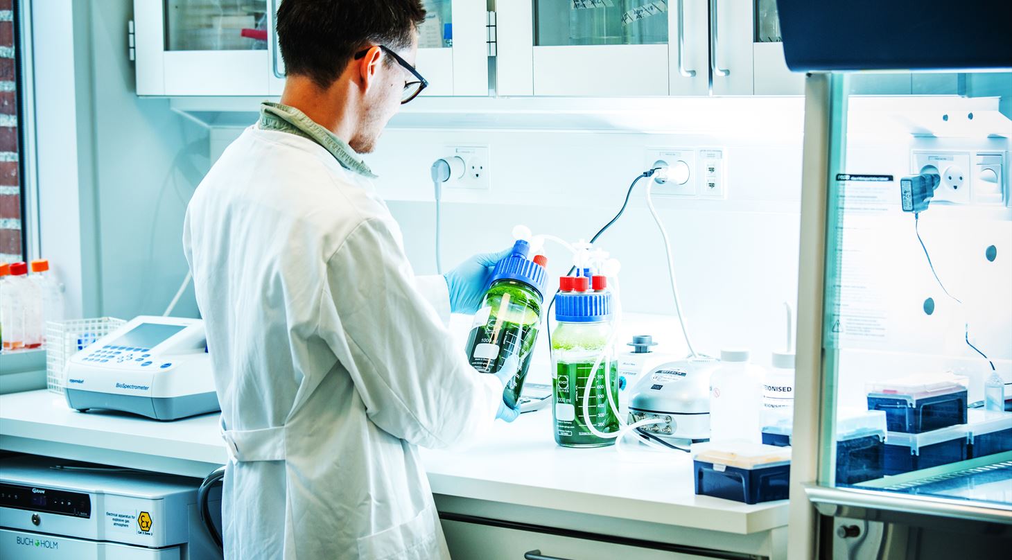Mand står i laboratioie, holder en 1 L mikroalge bioreactor