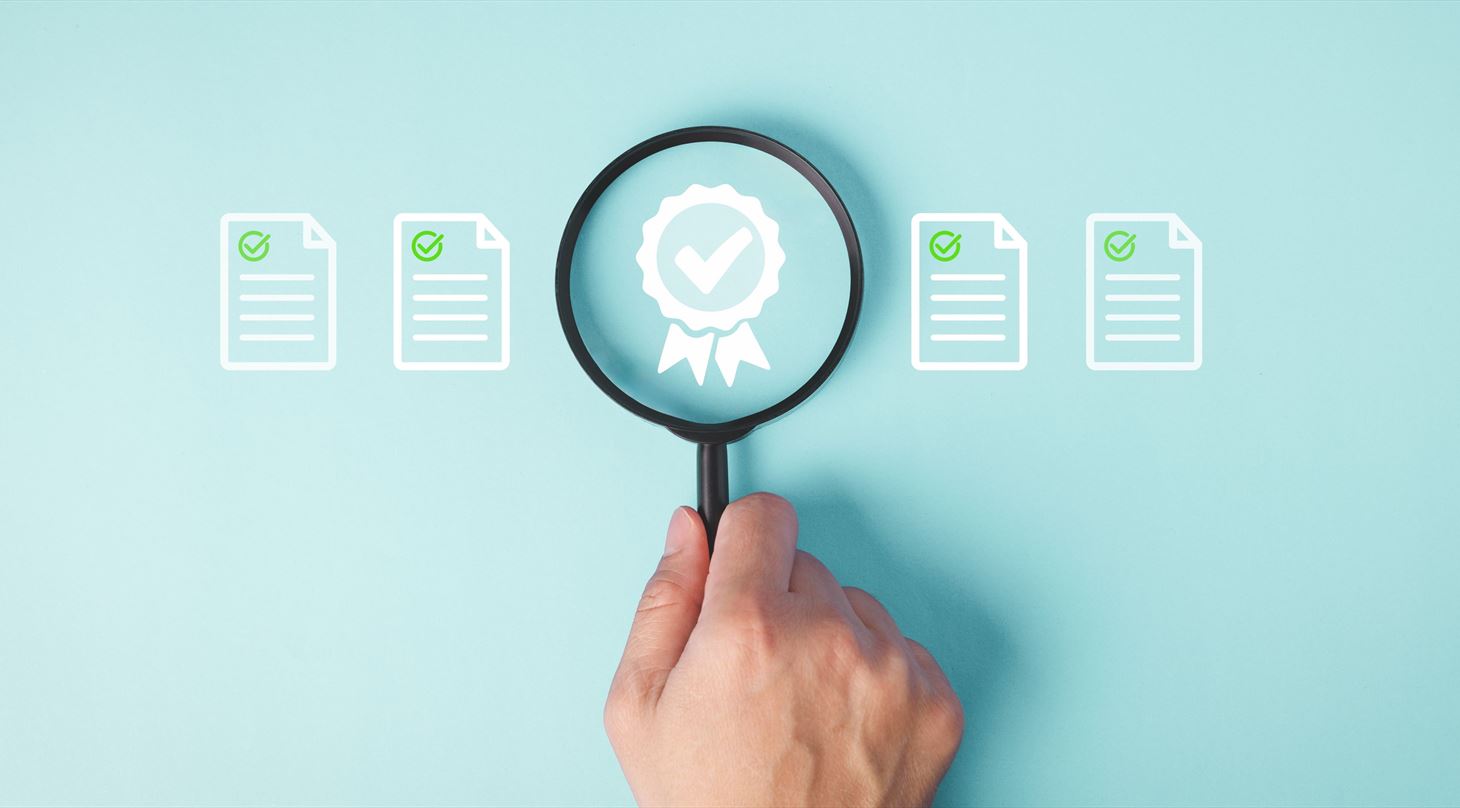 Licenseret
Hand Holding Magnifying Glass Over Quality Assurance Certificate to review and Approval Documents standard guarantee.
