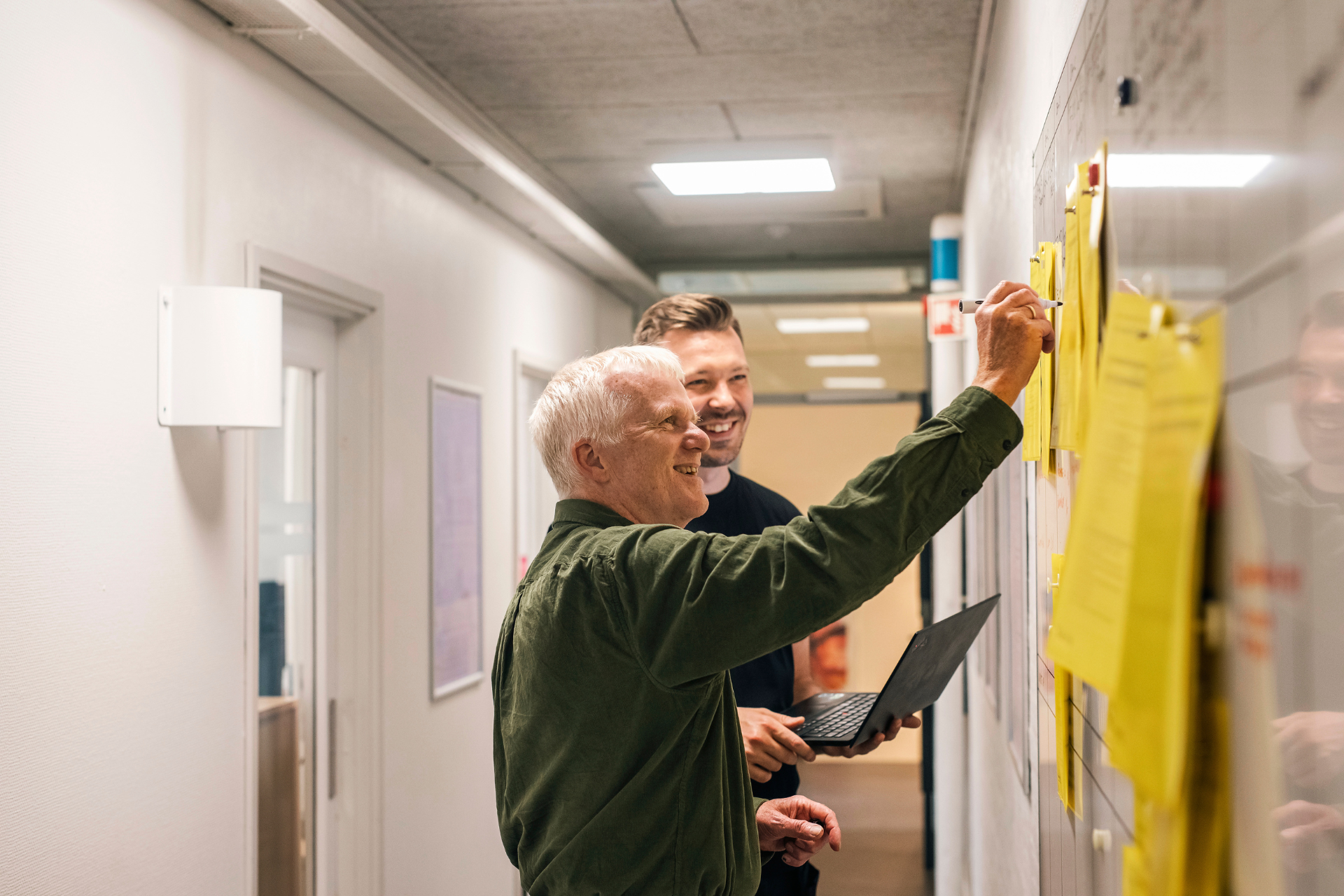 Billedet viser 2 personer, der er i gang med at planlægge test af varmepumper på Teknologisk Institut. De skriver på en tavle med gule mapper.