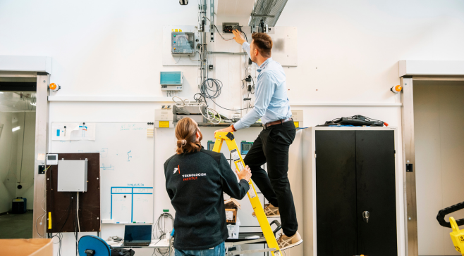 Two test engineers working in the Heat Pump Test Laboratoty. One is standing on a ladder and the other is holding the ladder.