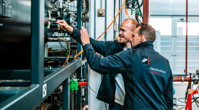 To teknikere der undersøger komponenter inde i en åben varmepumpe.
