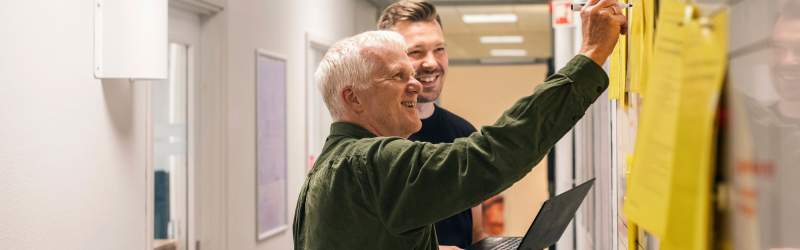 To smilende specialister der står og taler sammen på gangen i laboratoriebygningen.